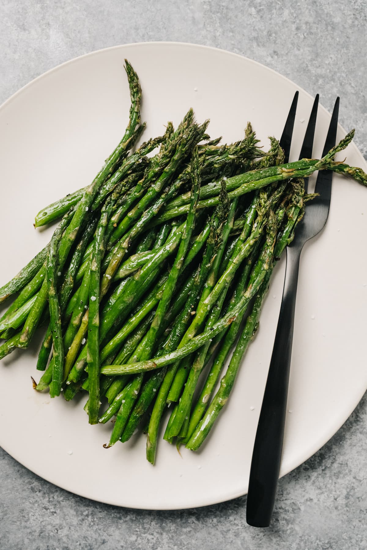 Air fryer asparagus on a cream plate with a silver serving fork on a concrete background.