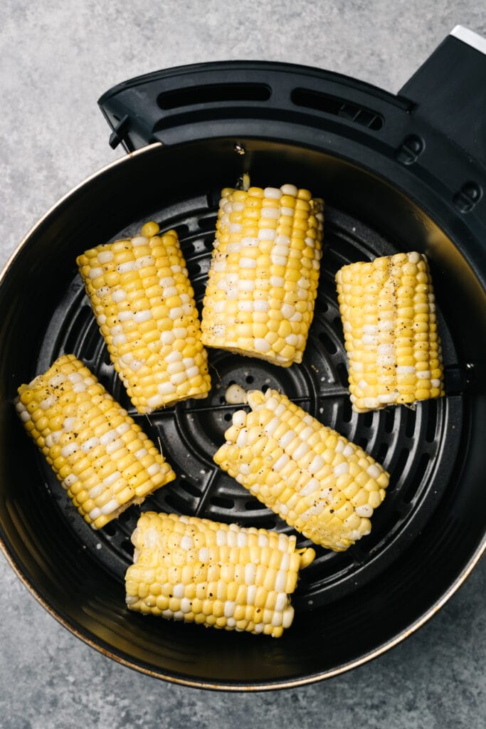 Raw corn on the cob rubbed with olive oil in a single layer in an air fryer basket.