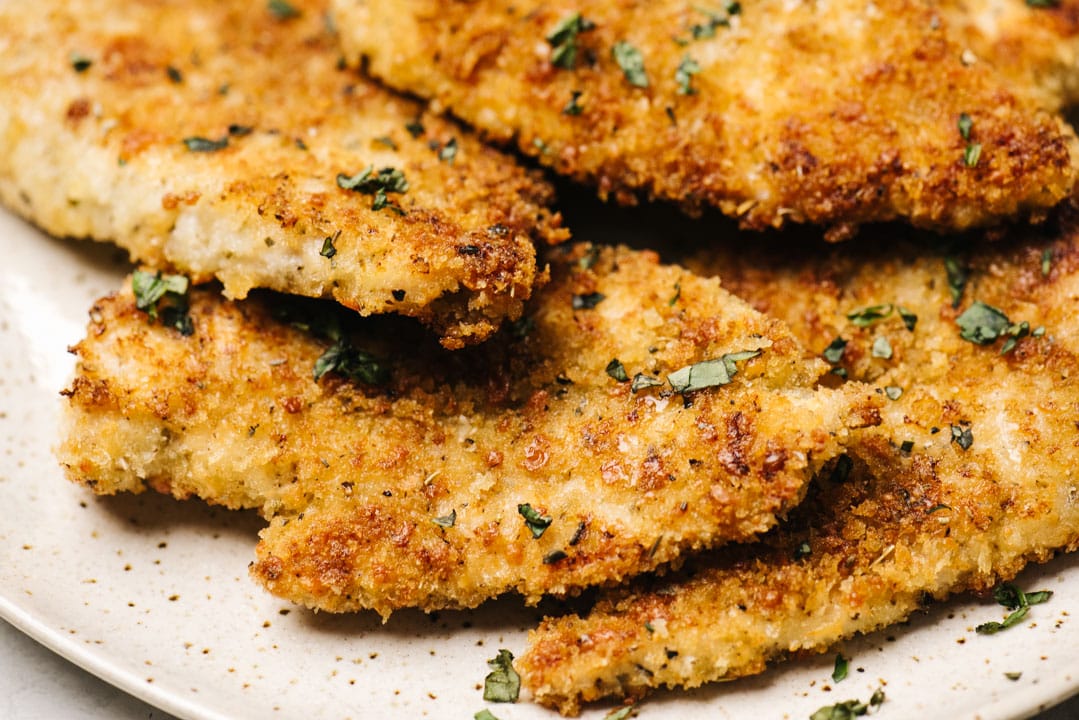 Side view, several parmesan crusted chicken breasts on a tan speckled serving platter.