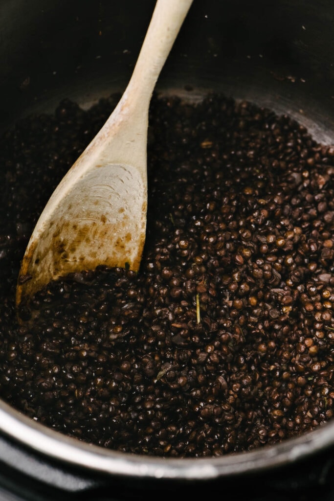 Side view, a wood spoon tucked into cooked black lentils in and Instant Pot.