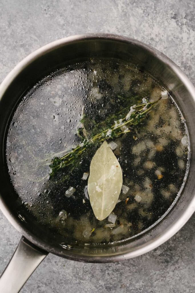 Sautéed onion and garlic with dried black lentils, water, thyme, and a bay leaf in a saucepot.