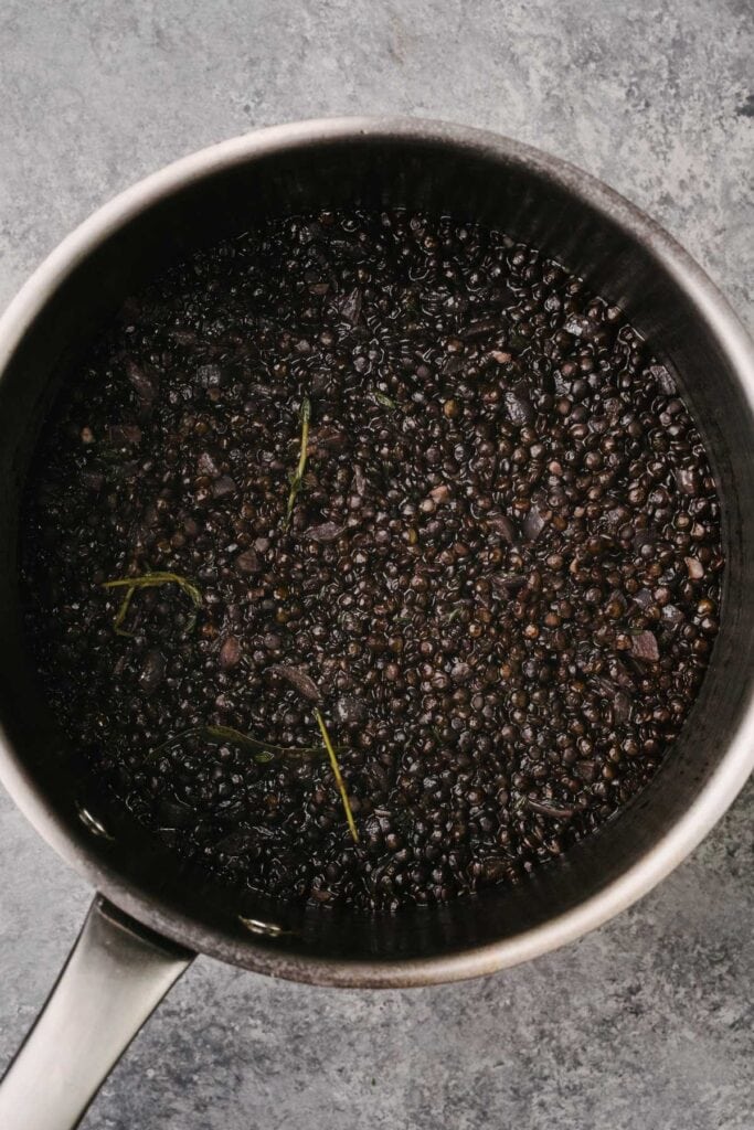 Cooked black lentils in a saucepan before draining the excess water.