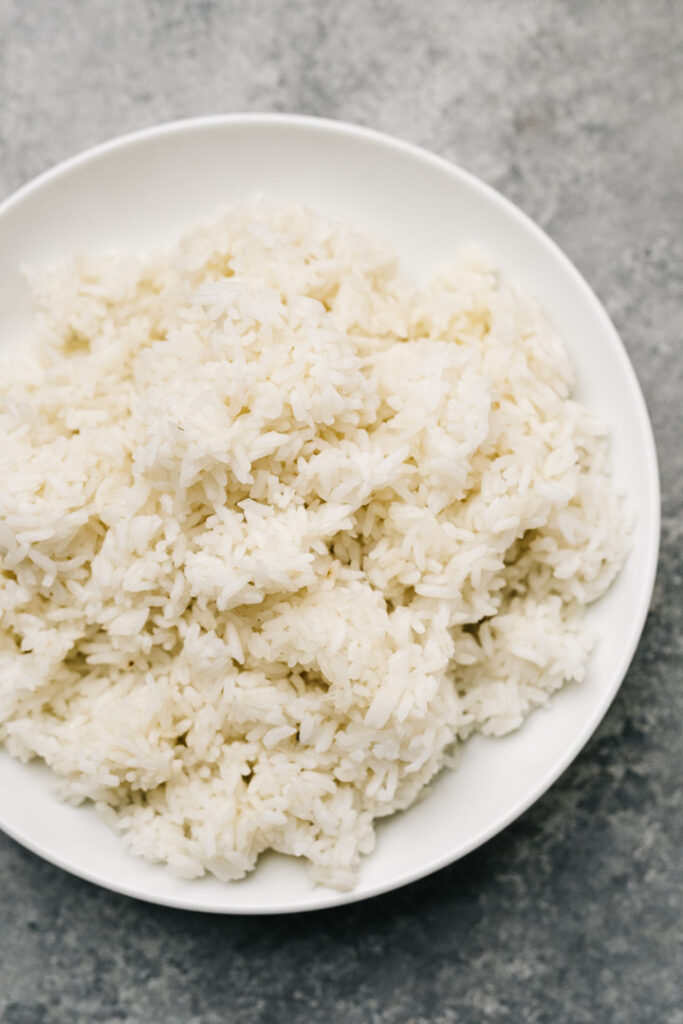 Day old white rice in a white bowl on a concrete background.