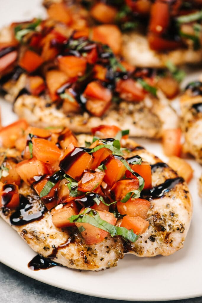 Side view, bruschetta chicken breasts on a cream serving platter, garnished with balsamic glaze.