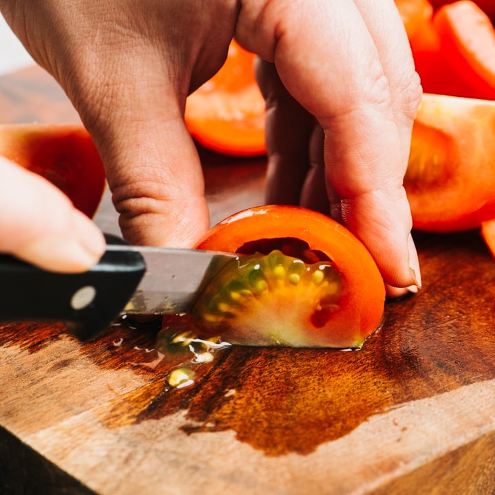 Removing the seeds from a quartered tomato on a cutting board.