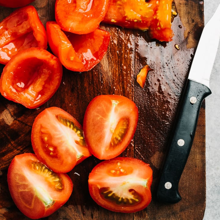 Quartered tomatoes on a cutting board, half with the seeds removed.