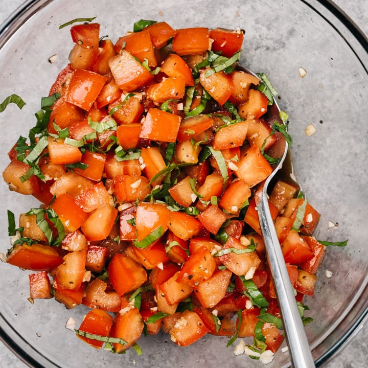 Tomato bruschetta in a glass mixing bowl - chopped tomatoes, garlic, salt, balsamic vinegar and fresh basil.