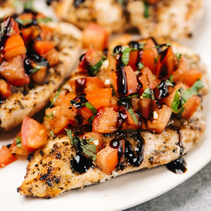 Side view, bruschetta chicken garnished with balsamic glaze on a cream serving platter.