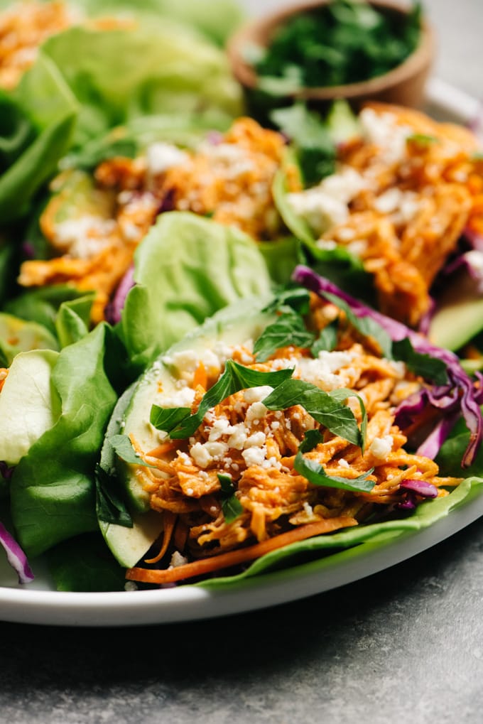 Side view, a platter of healthy buffalo chicken lettuce wraps with avocado and blue cheese crumbles.