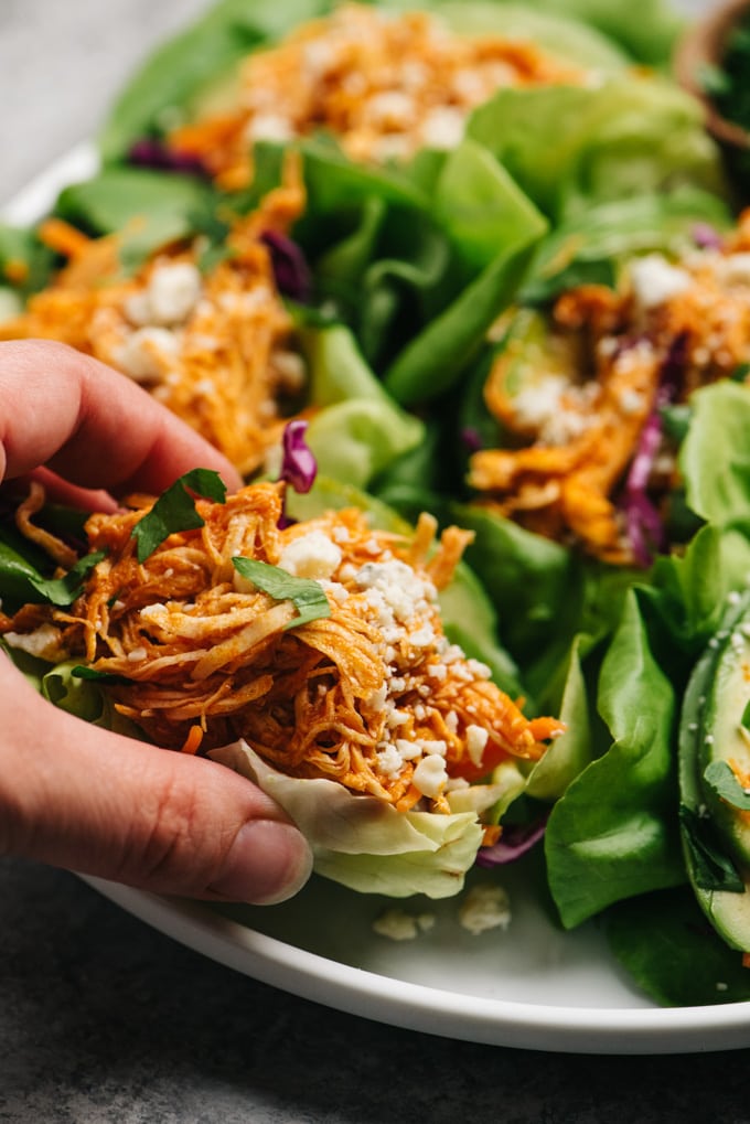 A woman's hand picking up a buffalo chicken lettuce wrap from a platter.