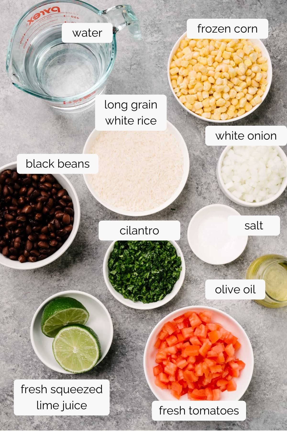 The ingredients to make tomato corn salsa and black beans and rice arranged in small bowls on a concrete background - frozen corn, tomatoes, white rice, black beans, onion, cilantro, lime juice, olive oil, and seasonings.