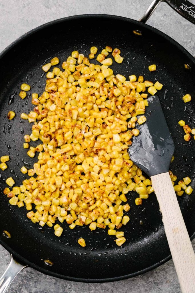 A spatula tucked into charred corn kernels in a skillet.