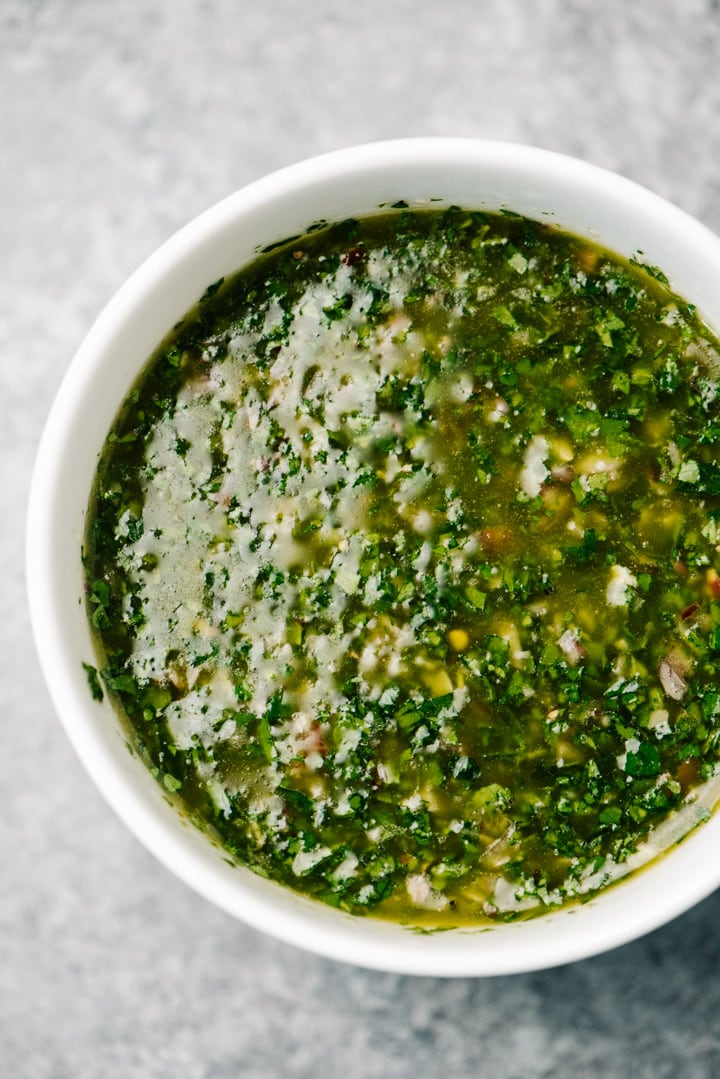 Chimichurri sauce in a white bowl on a concrete background.