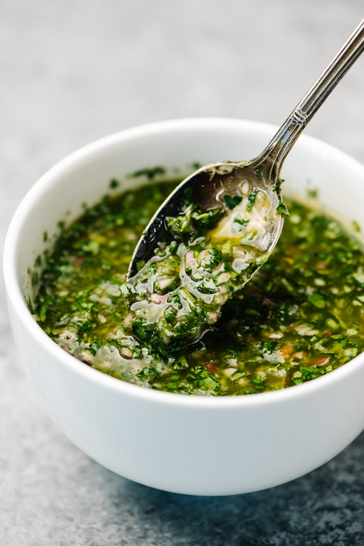 Chimichurri sauce running off a spoon over a white bowl.