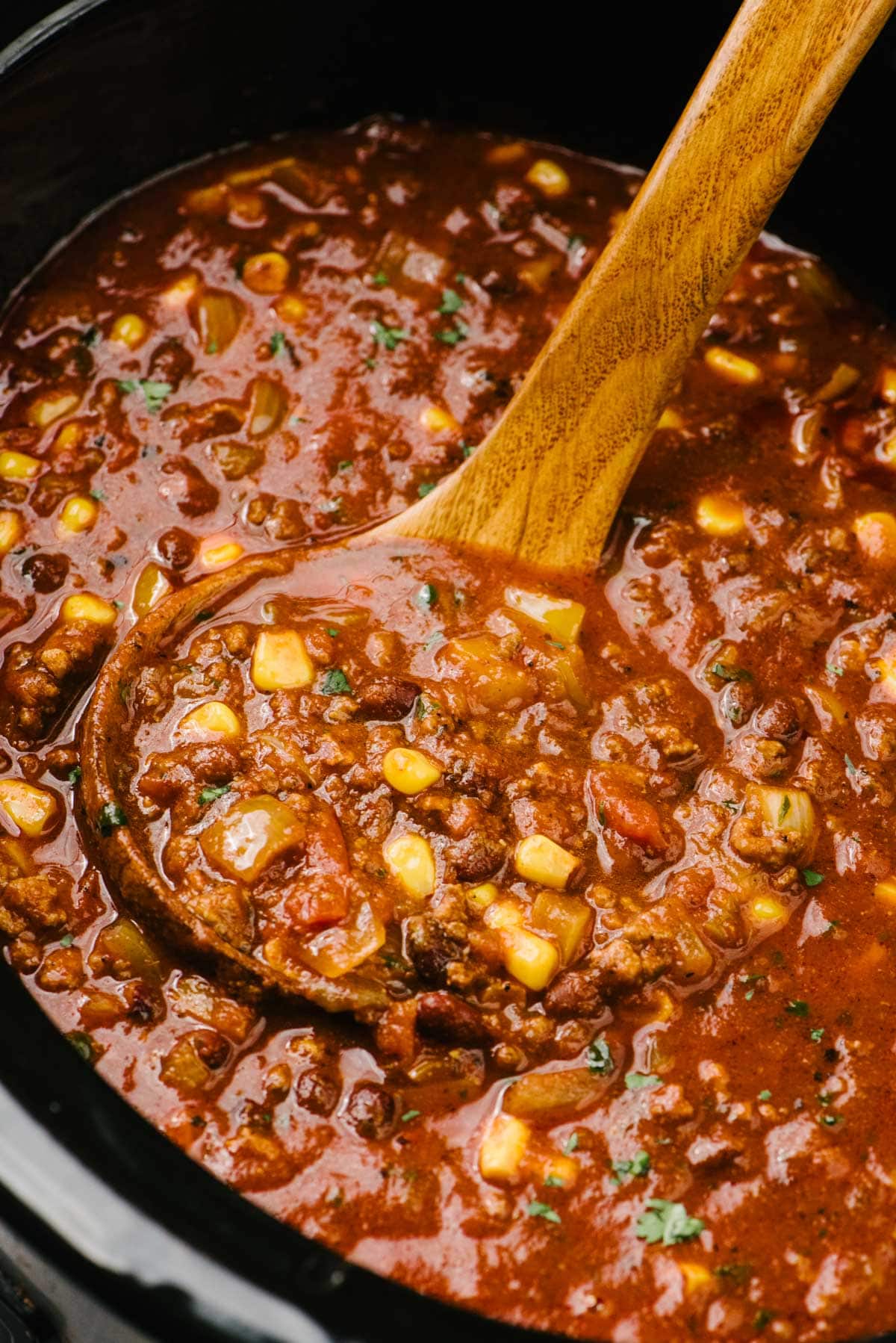 Side view, a wood ladle tucked into a slow cooker filled with taco soup.