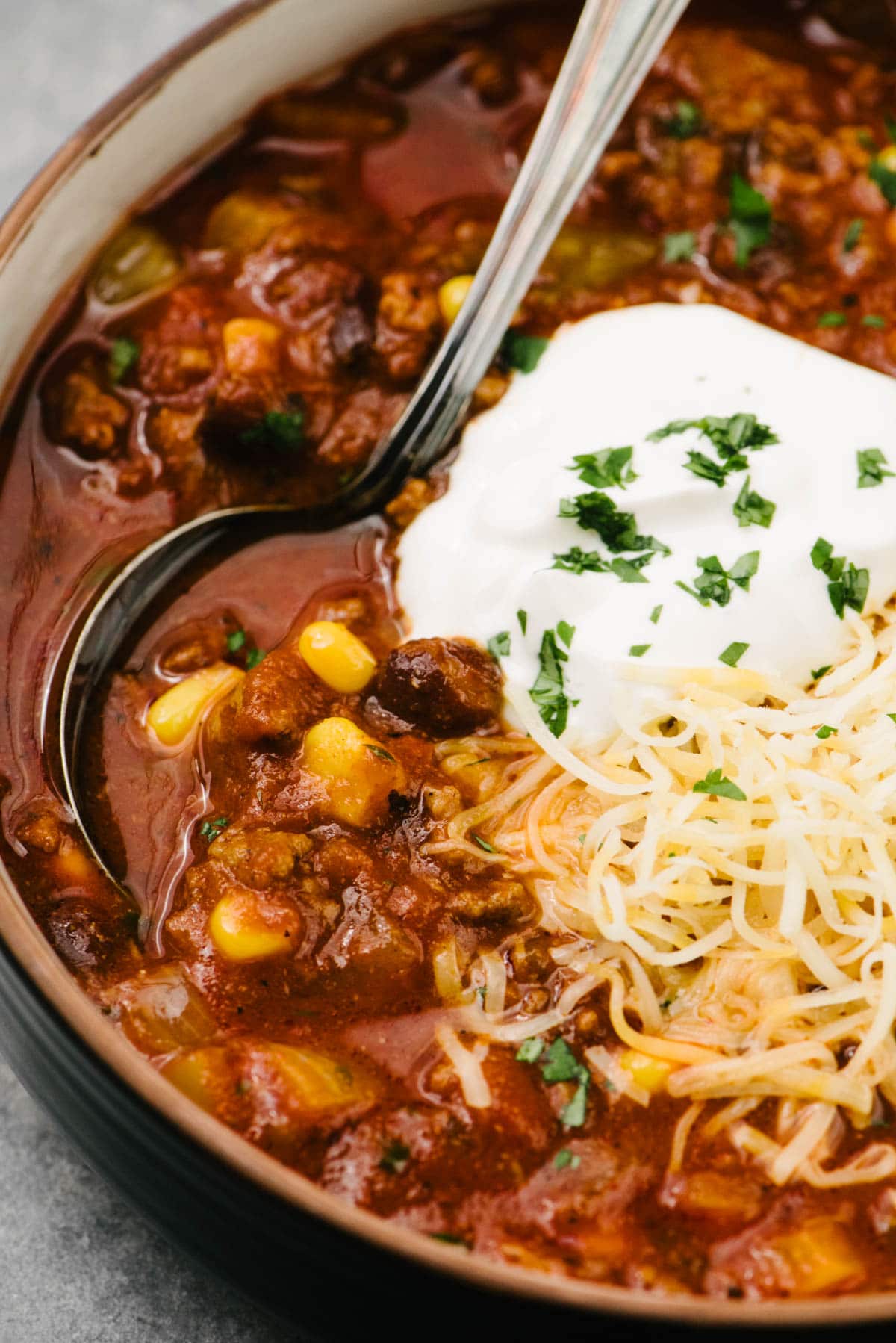 Side view, a spoon tucked into a bowl of crockpot taco soup, garnished with sour cream, shredded cheese, and fresh cilantro.