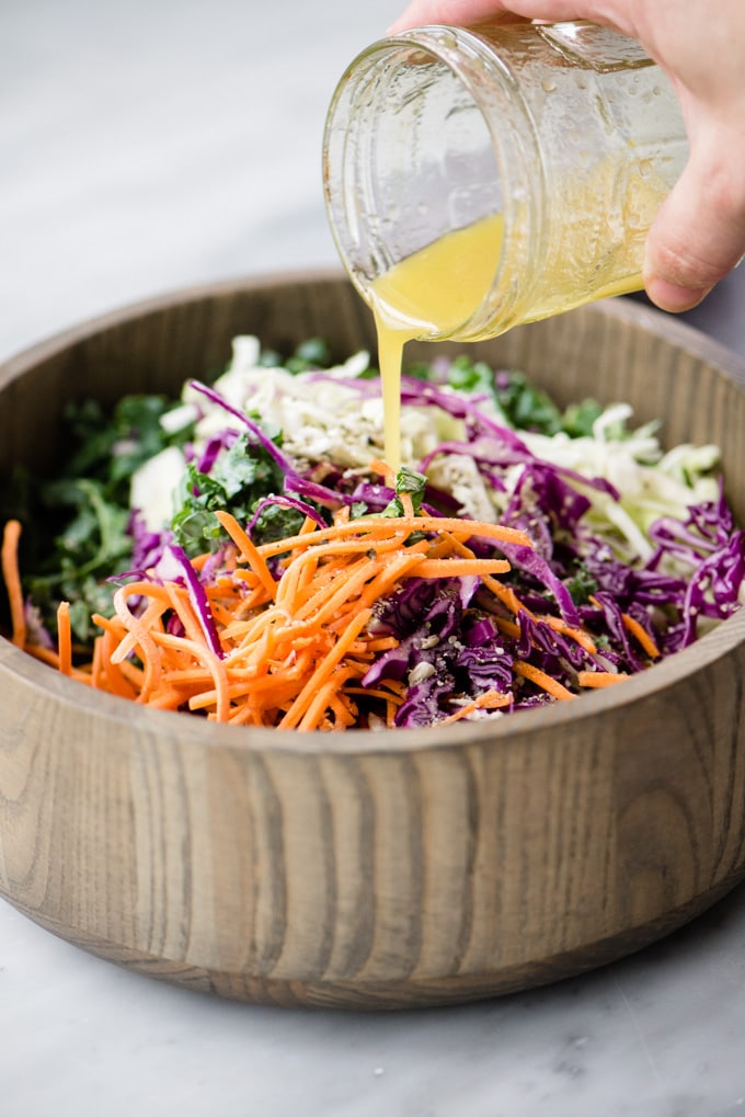 Adding apple cider dressing to a bowl of kale slaw.