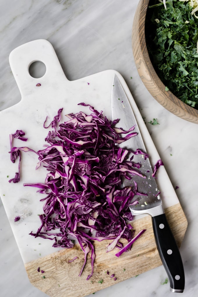 Thinly sliced red cabbage on a marble cutting board for kale slaw.