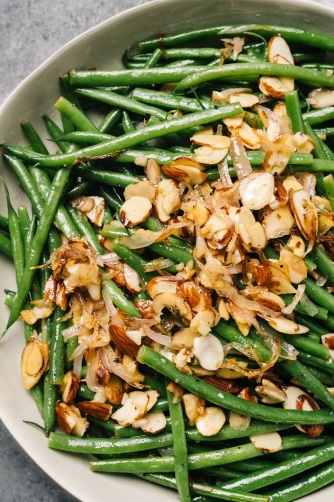 Green beans topped with buttered almonds in a tan serving bowl.