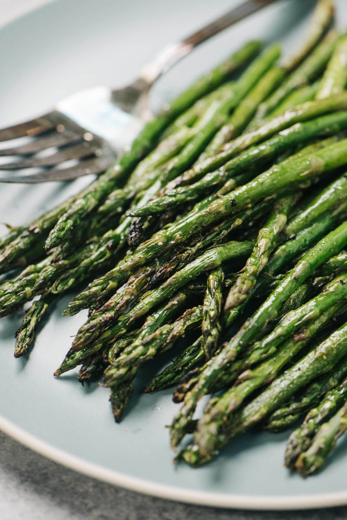 Side view, grilled asparagus on a blue plate with silver serving fork.