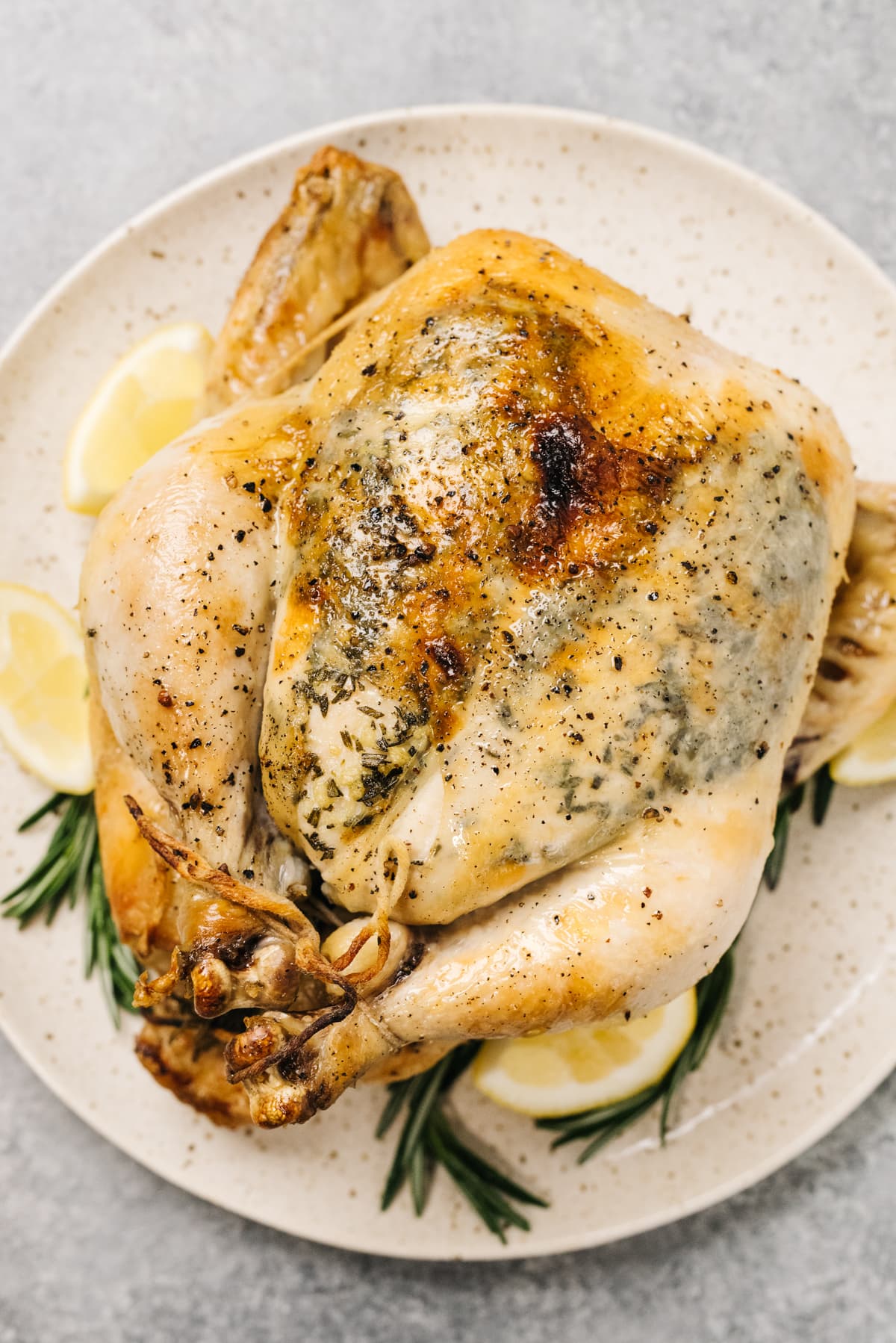 A slow cooker whole chicken on a platter with fresh herbs and lemon wedges for garnish.