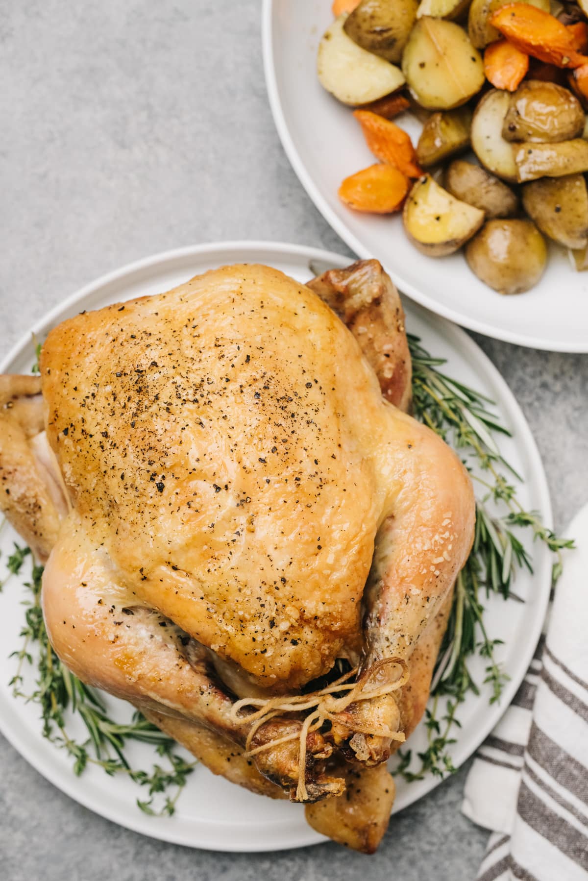 A whole roasted chicken on a white platter surrounded with fresh herbs for garnish.