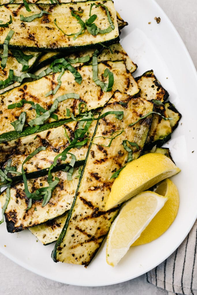 Grilled zucchini slices on a white platter with lemon wedges.