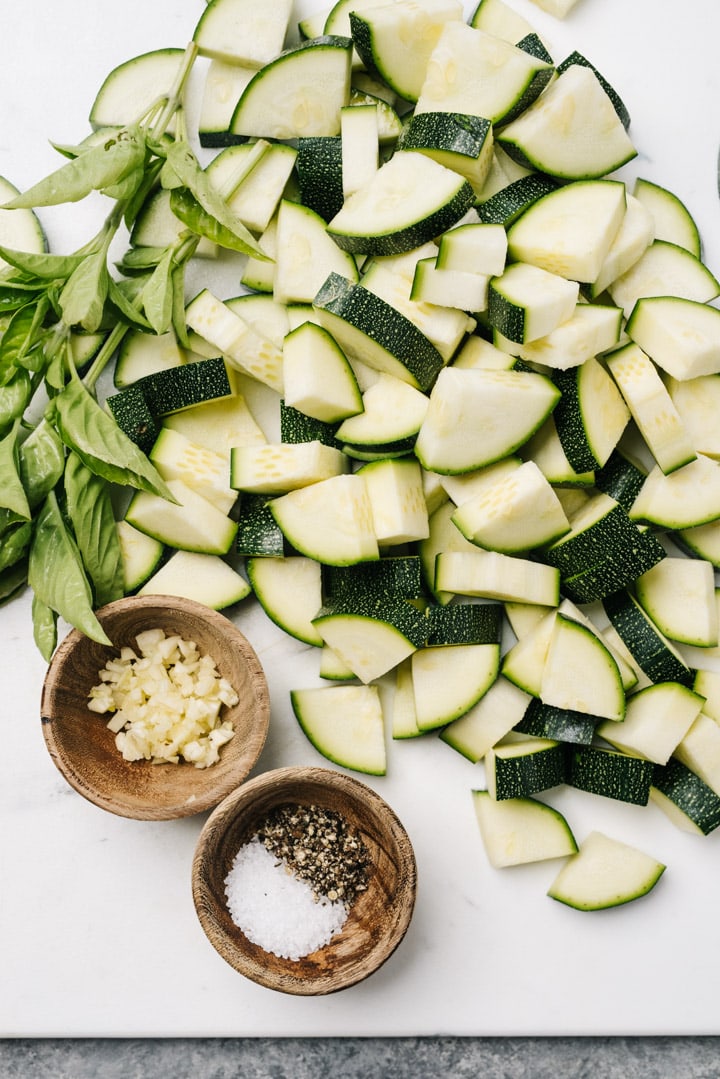 Chopped zucchini on a cutting baord with salt, pepper, garlic, and fresh herbs.