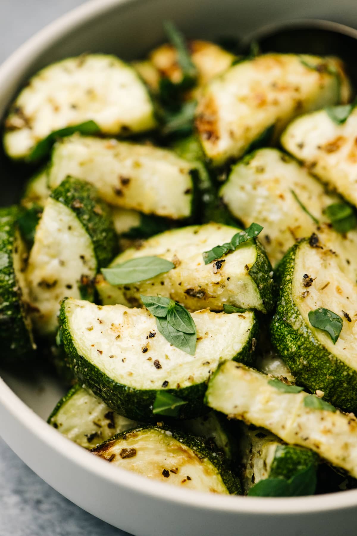 Side view, roasted zucchini in a tan serving bowl, garnished with fresh basil.