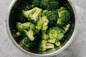 Broccoli florets tossed with olive oil and salt in a metal mixing bowl.