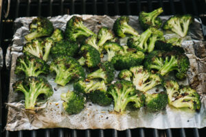 Grilled broccoli on a piece of foil over a grill grate.