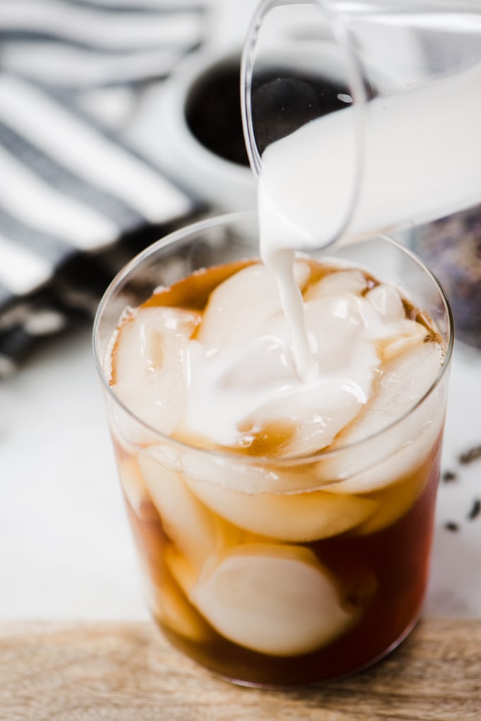 Pouring cashew milk or almond milk into an iced london fog tea latte.