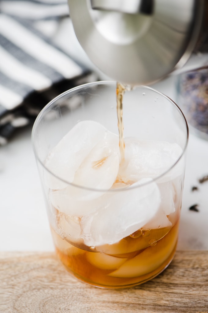 A woman pouring earl grey tea brewed with lavender into a glass of ice for a refreshing paleo london fog latte recipe.