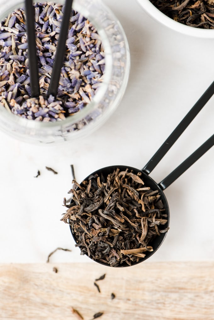 A tablespoon of loose leaf earl grey tea next to a small jar of lavender leaves for a london fog tea latte recipe.