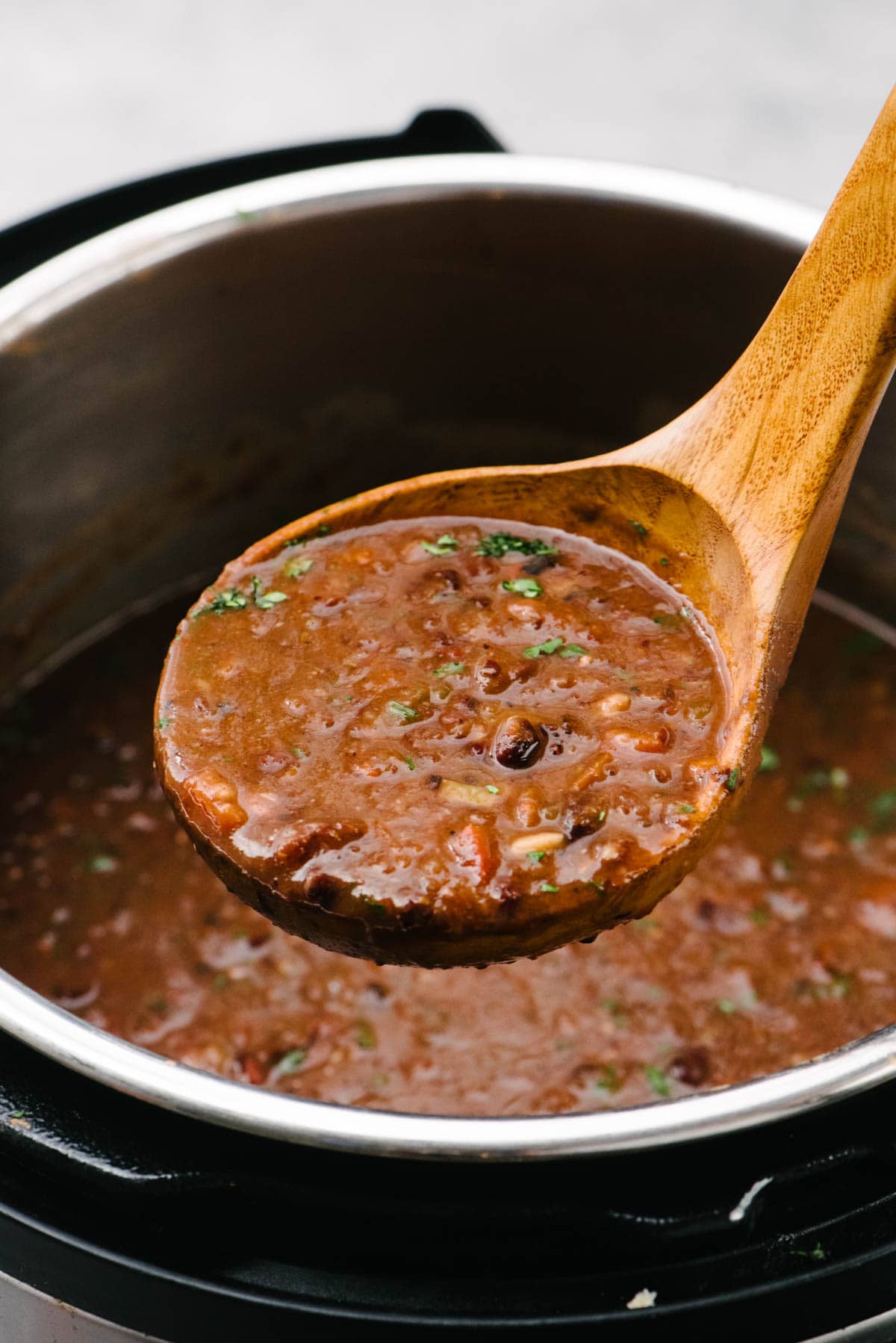 Side view, black bean soup in a wood ladle hovering over and Instant Pot.