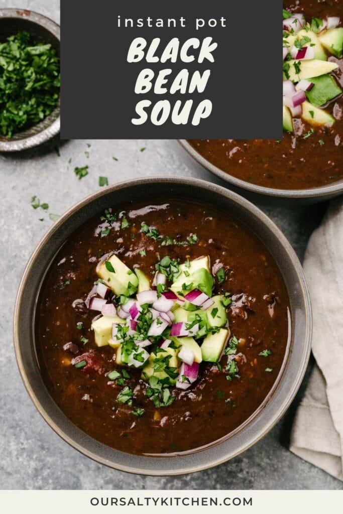 A bowl of Instant Pot black bean soup on concrete background garnished with diced red onion, diced avocado, and chopped cilantro; a tan linen napkin and two bowls of cilantro and avocado surround the bowl; title bar at the top reads "Instant Pot black bean soup".