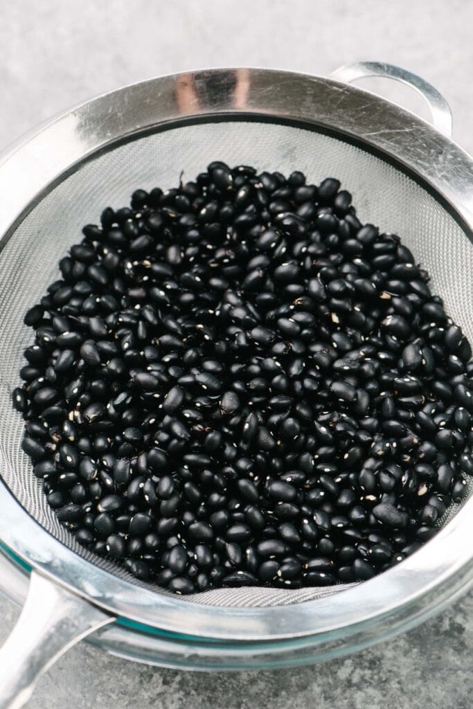 Dried black beans in a fine mesh strainer after being rinsed. 