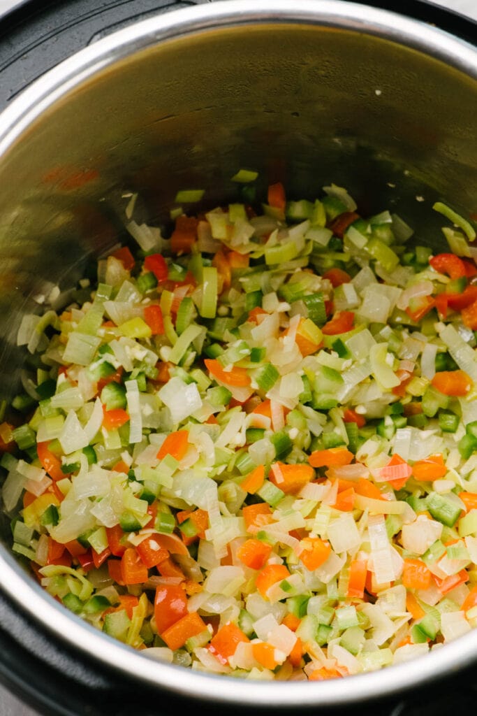 Side view, sautéed onions, leeks, celery, red bell pepper, minced jalapeño, and garlic in an Instant Pot.