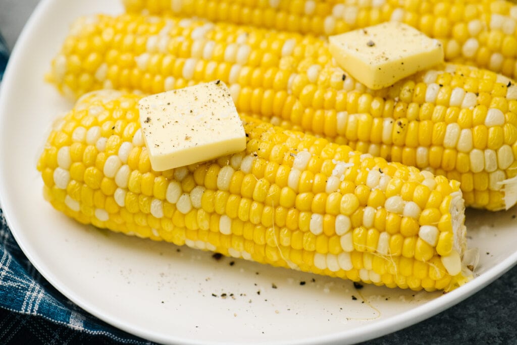 Side view, instant pot corn on the cob on a white plate topped with butter.