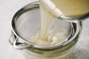 Straining chicken drippings through a fine mesh sieve nested in a 4-cup measuring cup.