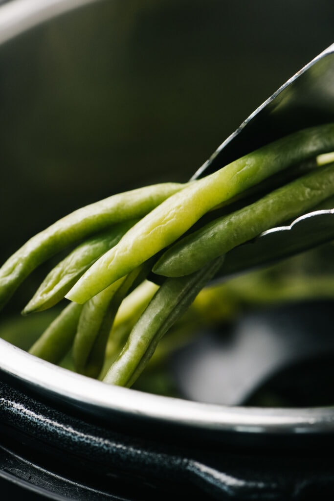 Tongs holding instant pot green beans.