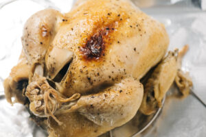 A whole chicken on a foil lined baking sheet after crisping skin under the broiler in the oven.