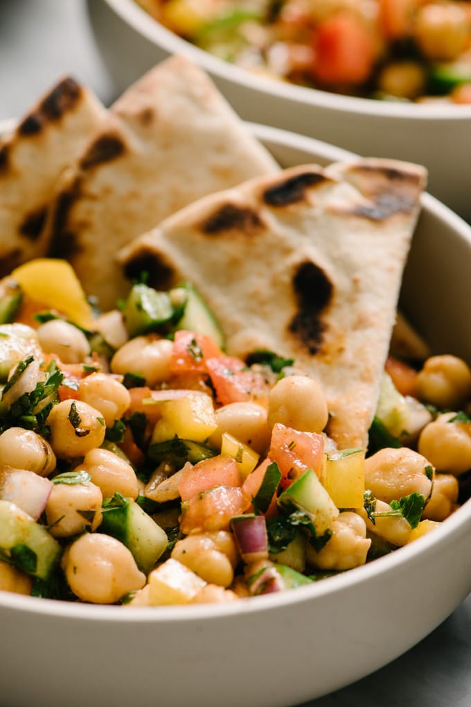 A bowl of mediterranean chickpea salad with several slices of pita bread tucked into the bowl.