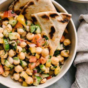 A bowl of vegan mediterranean chickpea salad with cucumber, tomato, bell pepper, mint, parsley, and lemon.