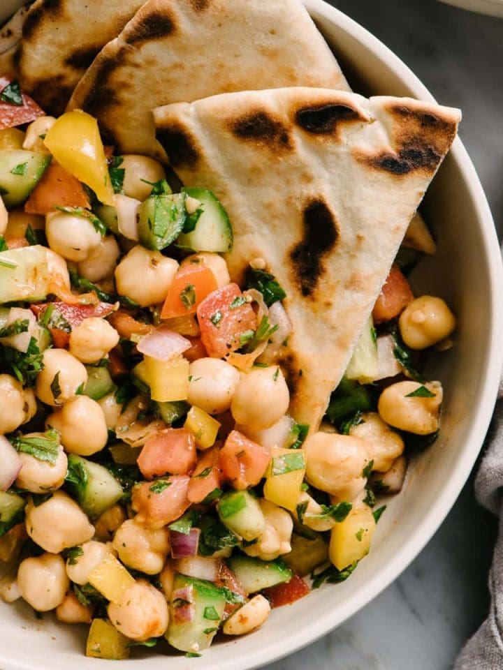 A bowl of vegan mediterranean chickpea salad with cucumber, tomato, bell pepper, mint, parsley, and lemon.