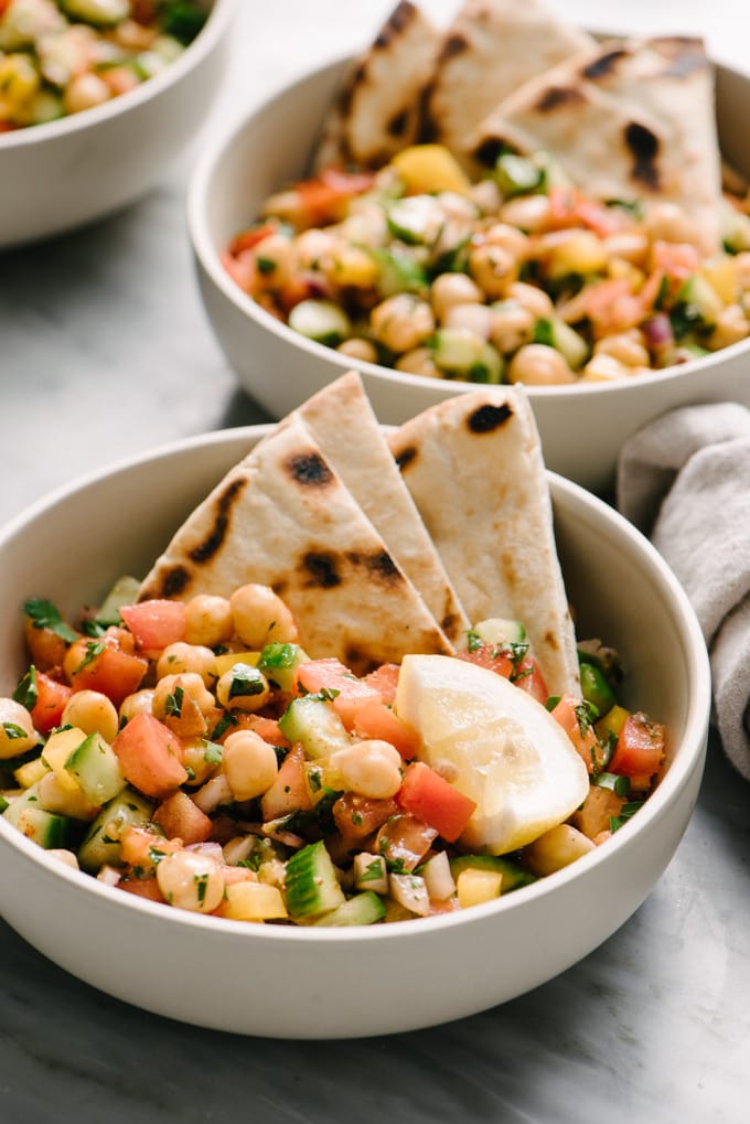 Three bowls of vegan mediterranean chickpea salad on a marble table. 