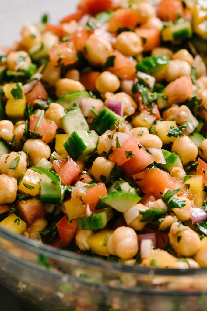 A close-up image mediterranean chickpea salad showing the individual ingredients - marinated chickpeas, cucumber, tomato, bell pepper, red onion, mint, and parsley.