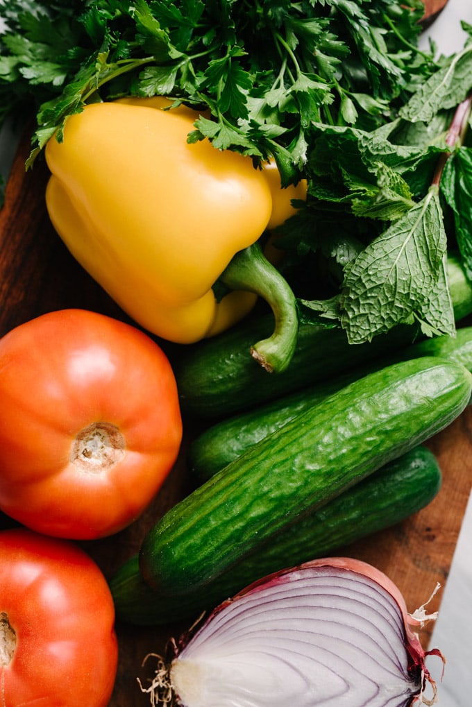 Whole vegetables and herbs for making mediterranean chickpea salad on a cutting board.