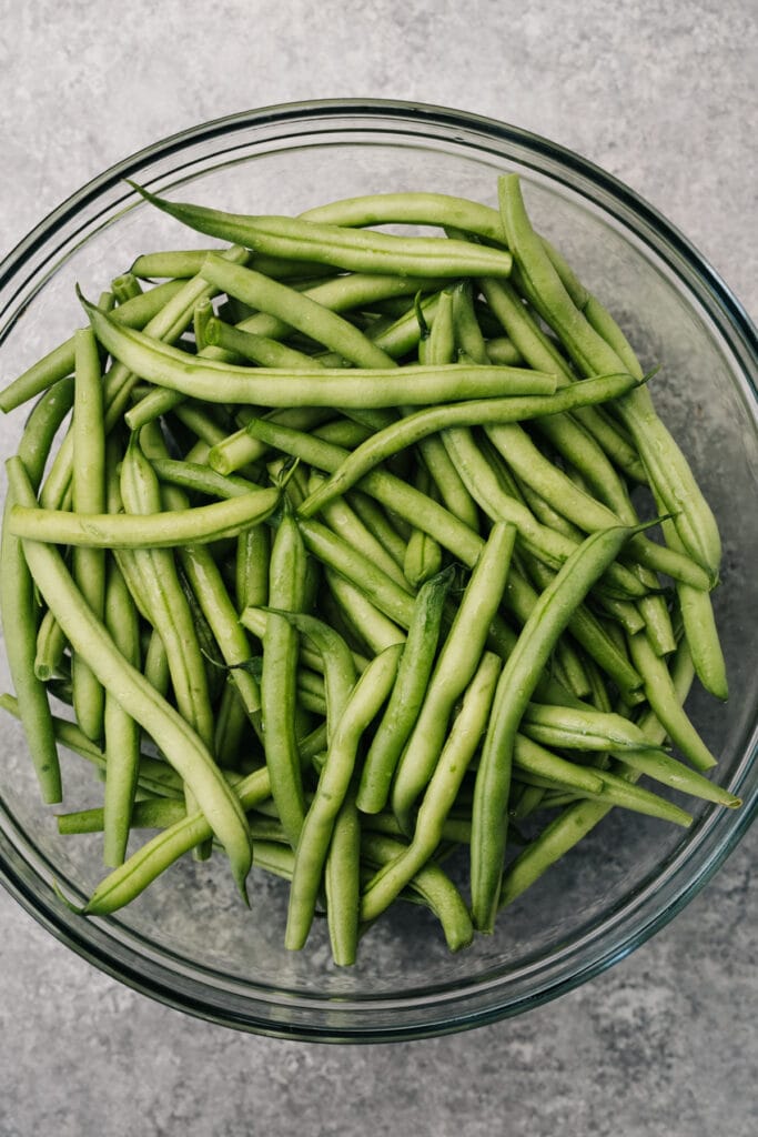 Raw green beans with water in glass microwave safe bowl.