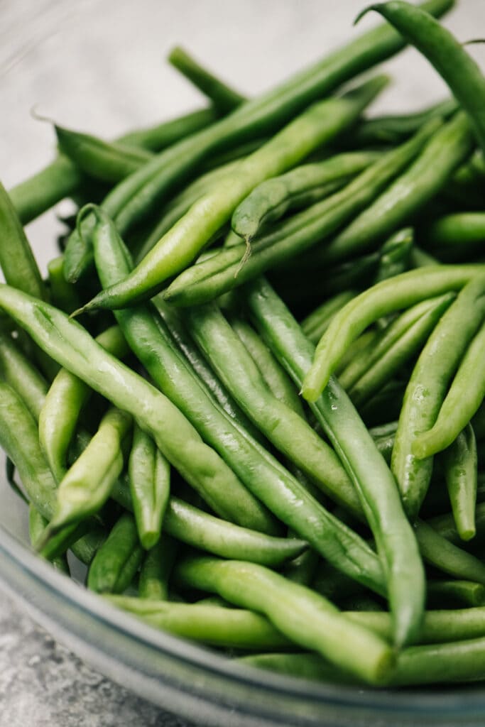 Side view, steamed green beans and water in a microwave safe bowl.